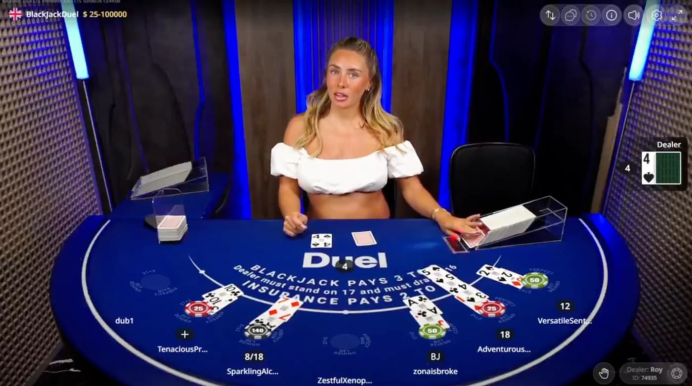 English adult performer Bonnie Blue dealing at a Duel live blackjack table on June 2, 2026, surrounded by player seats and chips with the Duel branded felt and 3 to 2 payout signage.